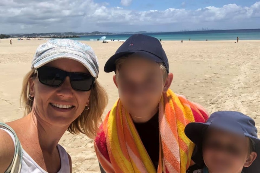 A woman in sunglasses  with the kids at the beach.