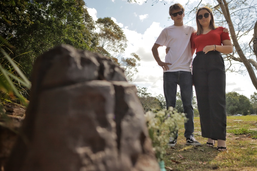 Two young adults look at a rock with flowers.