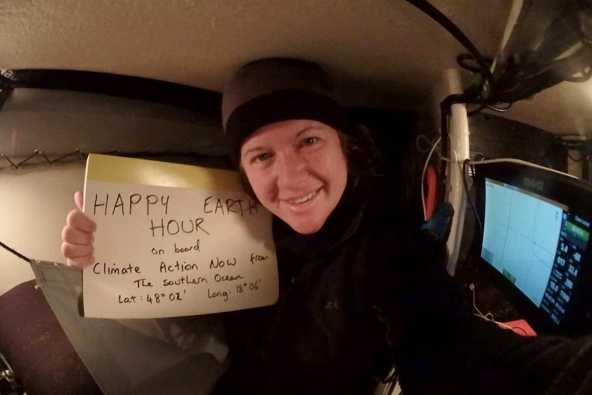 Lisa Blair holds a sign reading HAPPY EARTH HOUR sitting in the hull of her boat.