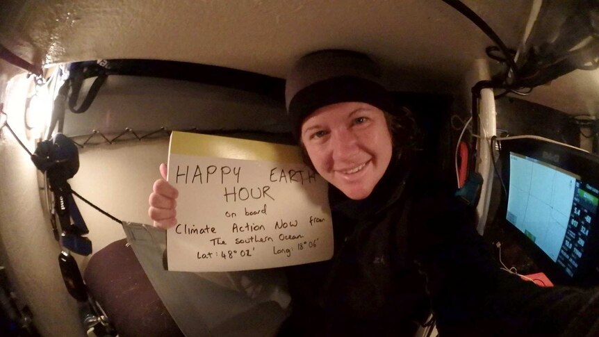 Lisa Blair holds a sign reading HAPPY EARTH HOUR sitting in the hull of her boat.