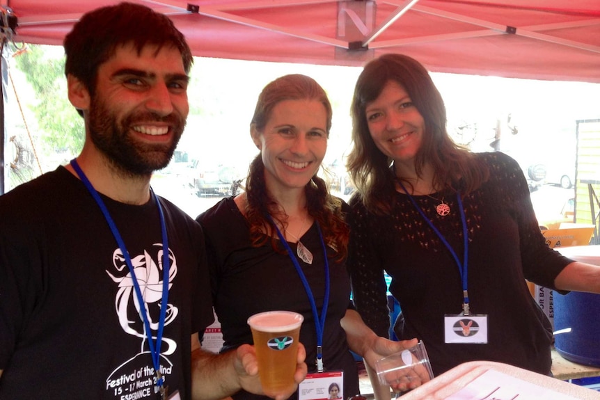 Two women and one man inside a tent holding a freshly poured beer