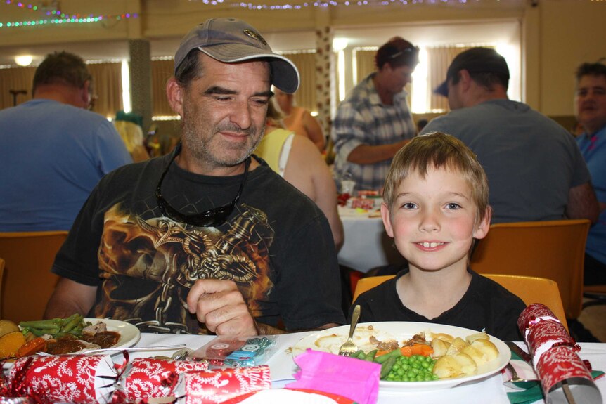Father and son eat a soup kitchen Christmas meal.