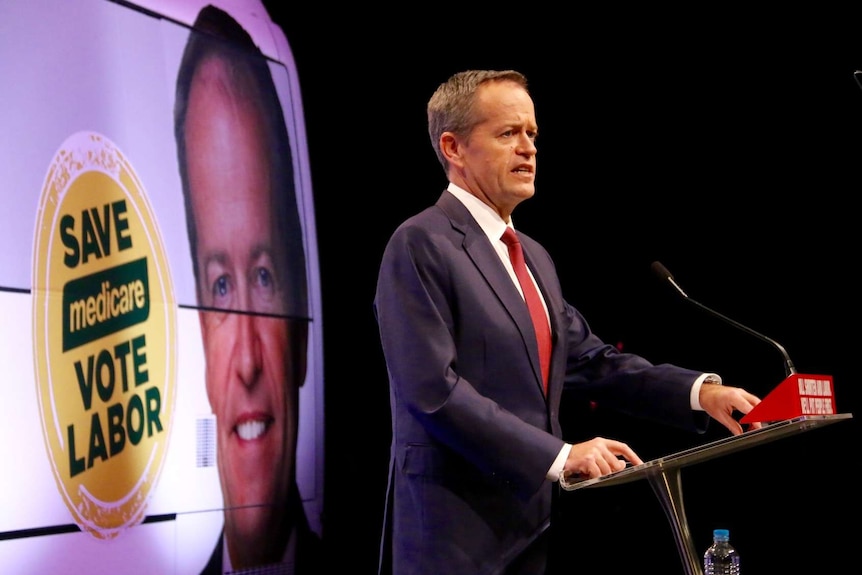 Bill Shorten speaks at a podium. A sign in the background says save Medicare vote Labor