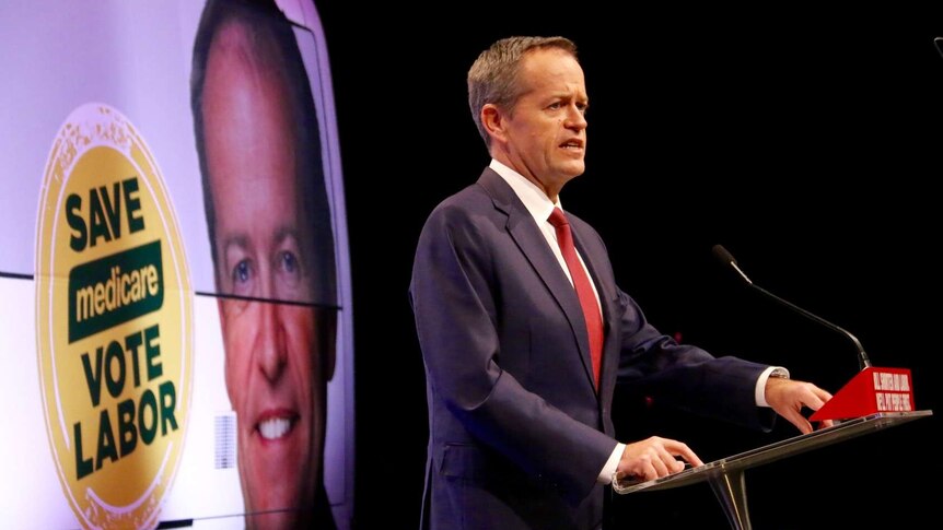 Bill Shorten speaks at a podium. A sign in the background says save Medicare vote Labor