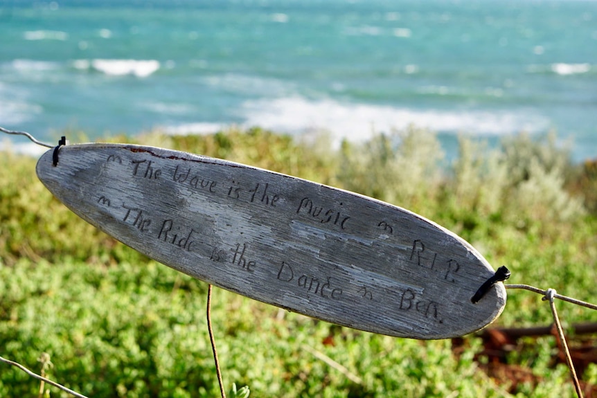 A wooden memorial shaped like a surf board attached to a fence near where Ben Gerring was fatally attacked by a shark