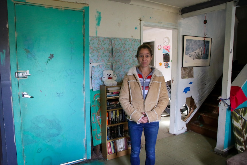 Heike Ignjatovic stands inside her public housing home, the interior appears rundown.