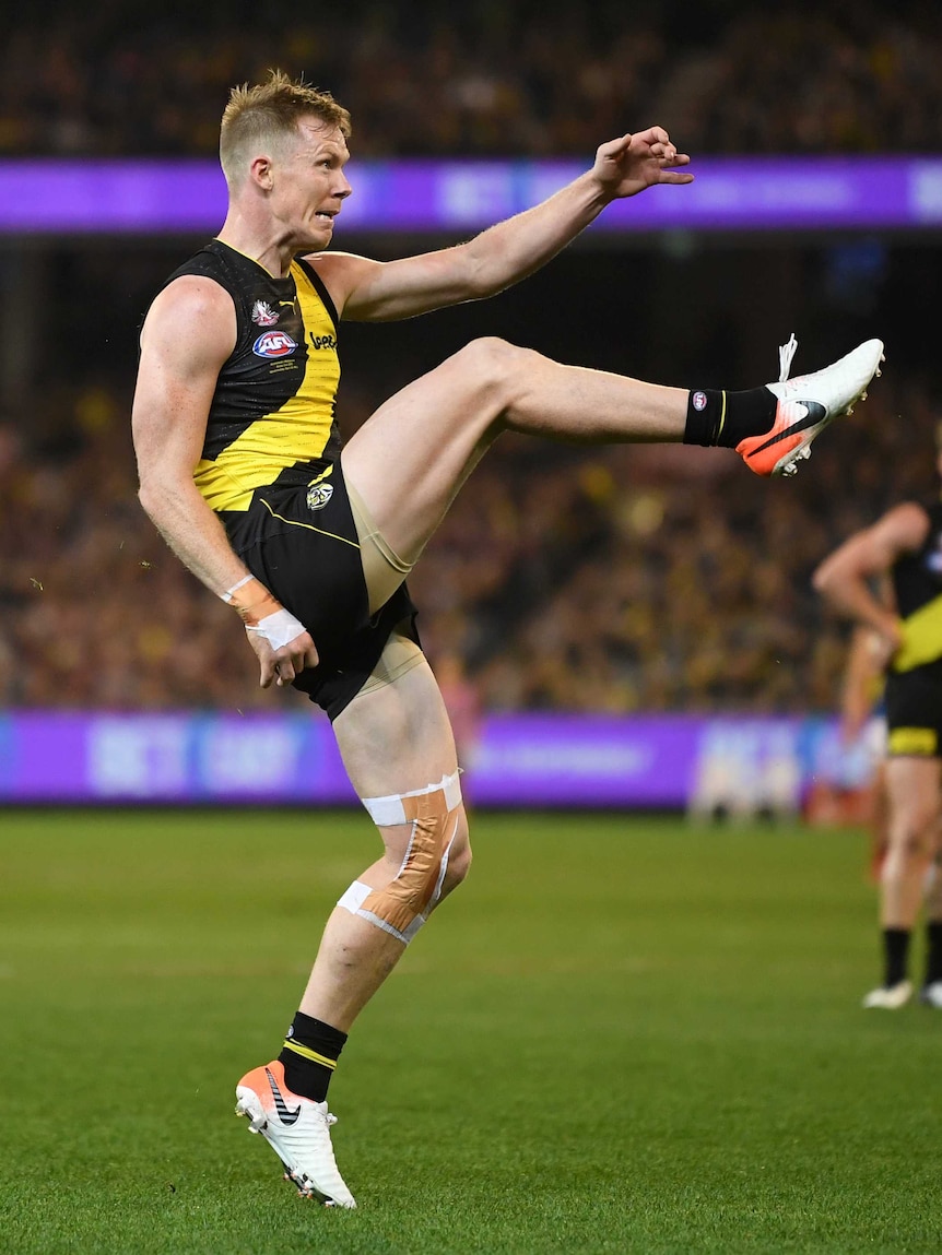 An AFL player lifts his leg high as he kicks for goal