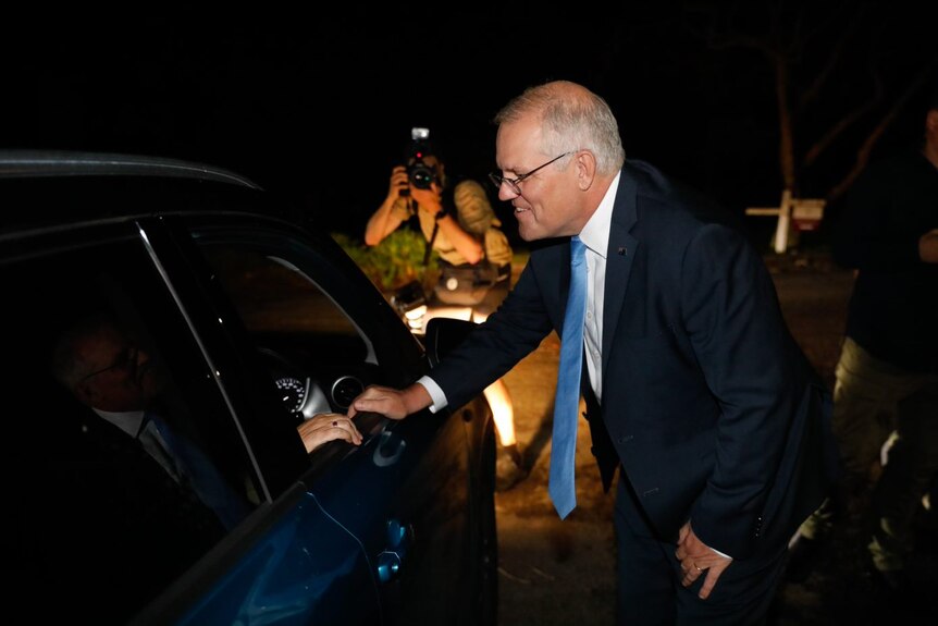 Prime Minister Scott Morrison leans into a car while its dark outside.