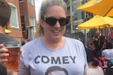 Angela wears a grey t-shirt that reads 'Comey is my Homey' while holding a pint of beer.