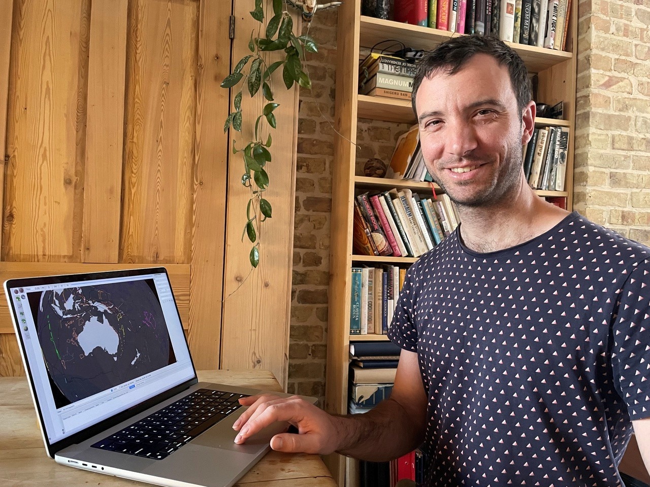 Ben Mather sits in an office in casual clothes, in front of a computer showing a map of Australia.