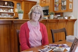 A woman sits at her kitchen table with old photos spread in front of her.