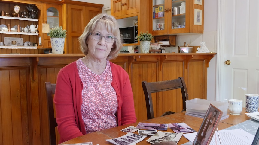 A woman sits at her kitchen table with old photos spread in front of her.