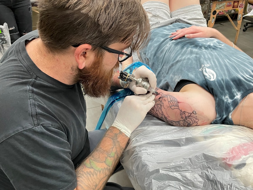 A man tattooing someon's shoulder. 