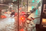 Cars at a standstill in a flooded street where red traffic lights reflect off the water.