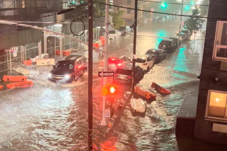 Cars at a standstill in a flooded street where red traffic lights reflect off the water.