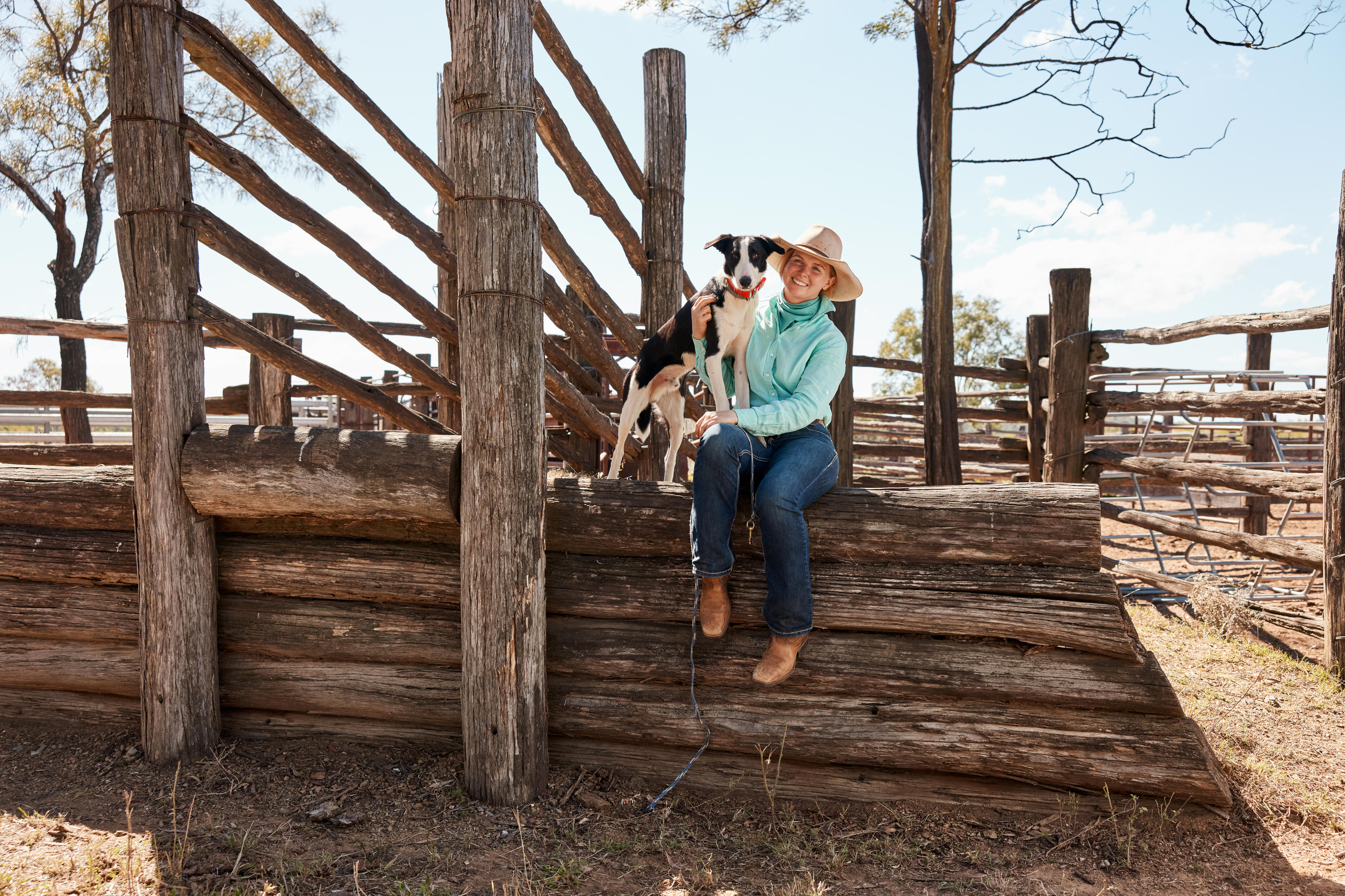 A dog stands near a woman as she sits on an old wooden cattle loading ramp.