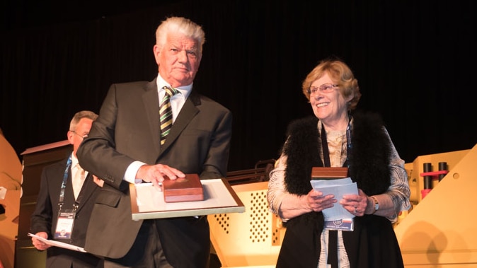 A man in a suit receives an award from a woman. 