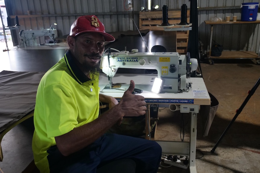 Edwin Turner gives a thumbs up while sitting down at a sowing machine in the swag workshop in Katherine.