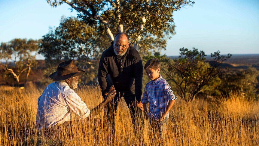 Devon Cuimara and his son Djeran stand in a field of long grass with Martu elder Colin Peterson.