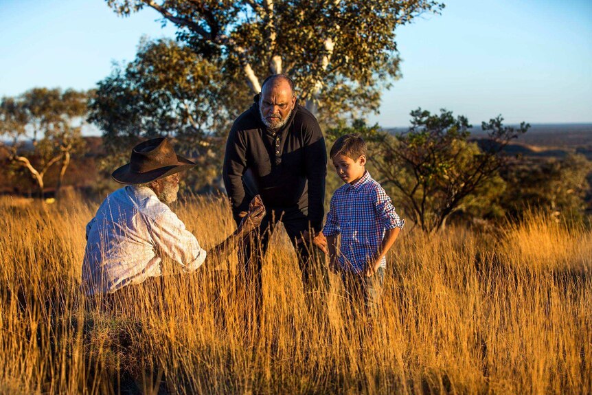 Devon Cuimara and his son Djeran stand in a field of long grass with Martu elder Colin Peterson.