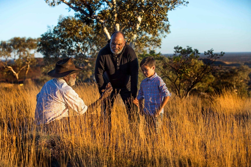 Devon Cuimara and his son Djeran stand in a field of long grass with Martu elder Colin Peterson.