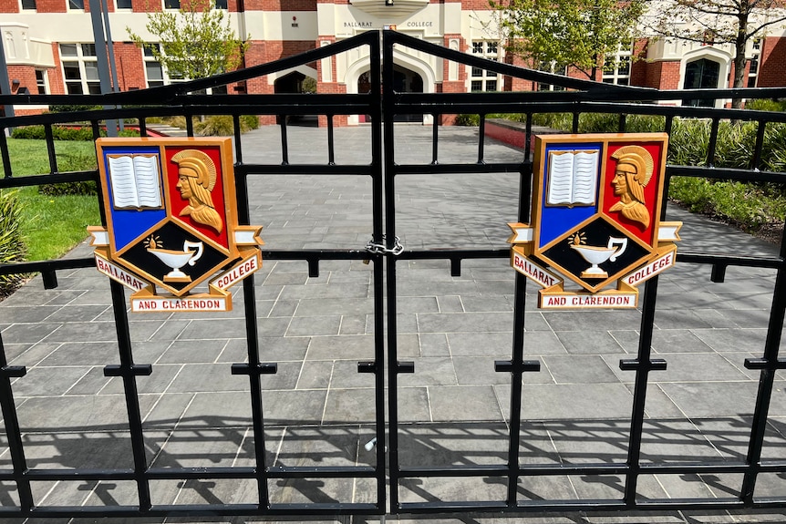 Locked iron gates with a black, red and blue crest, behind lies lawns and a red and cream Victorian building.