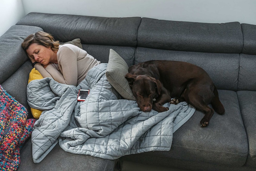 Woman asleep on a sofa with a pet dog lying over her legs