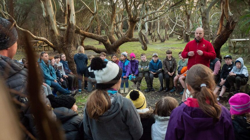 Jarrod Edwards, welcomes an encircled group of  kids on country, under sheltering gum trees