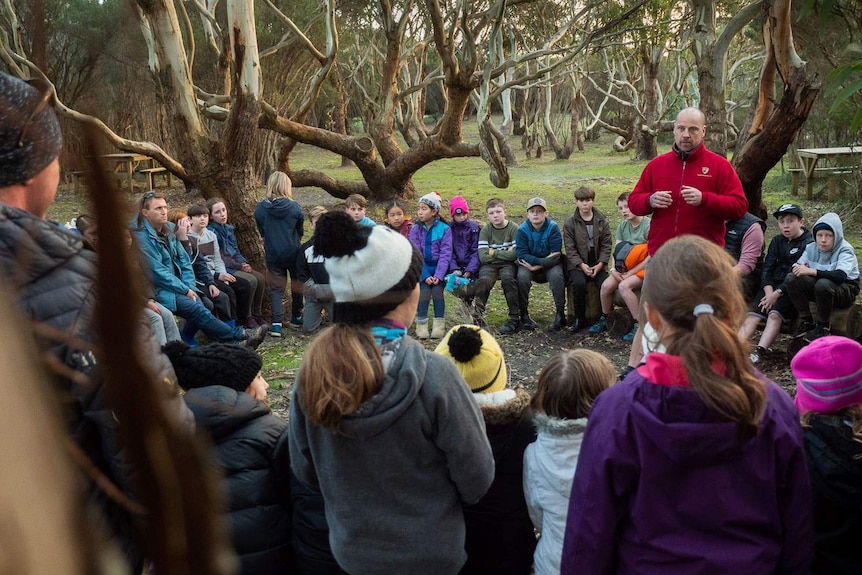 Jarrod Edwards, welcomes an encircled group of  kids on country, under sheltering gum trees