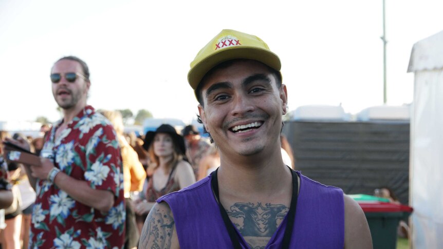 Man wearing a purple vest and yellow cap smiling at the camera