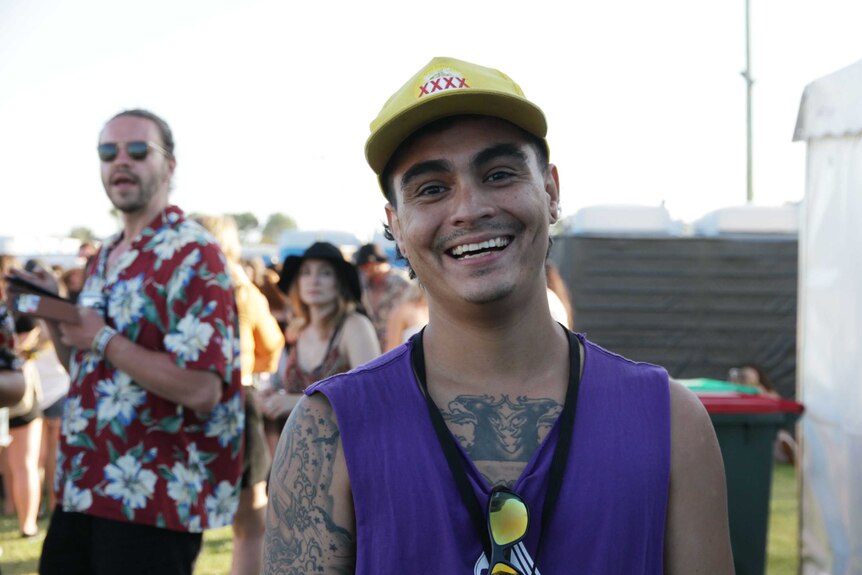 Man wearing a purple vest and yellow cap smiling at the camera