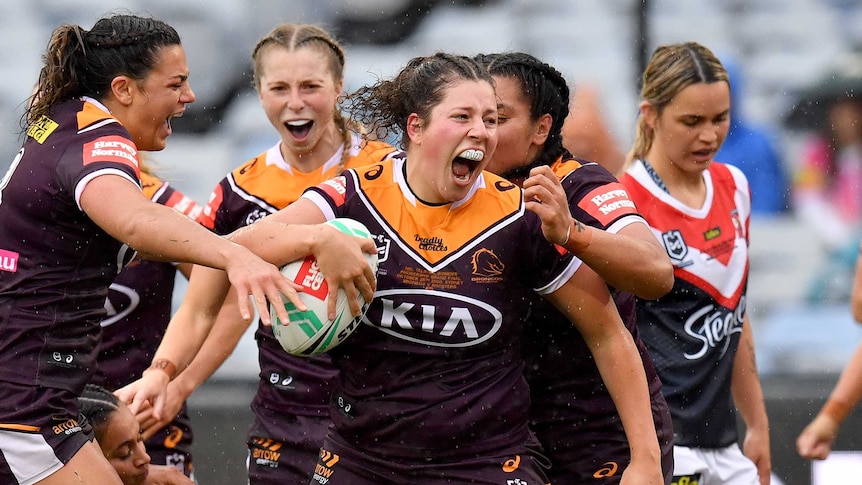 Chelsea Lenarduzzi screams and holds the rugby ball under her arm as teammates celebrate behind her