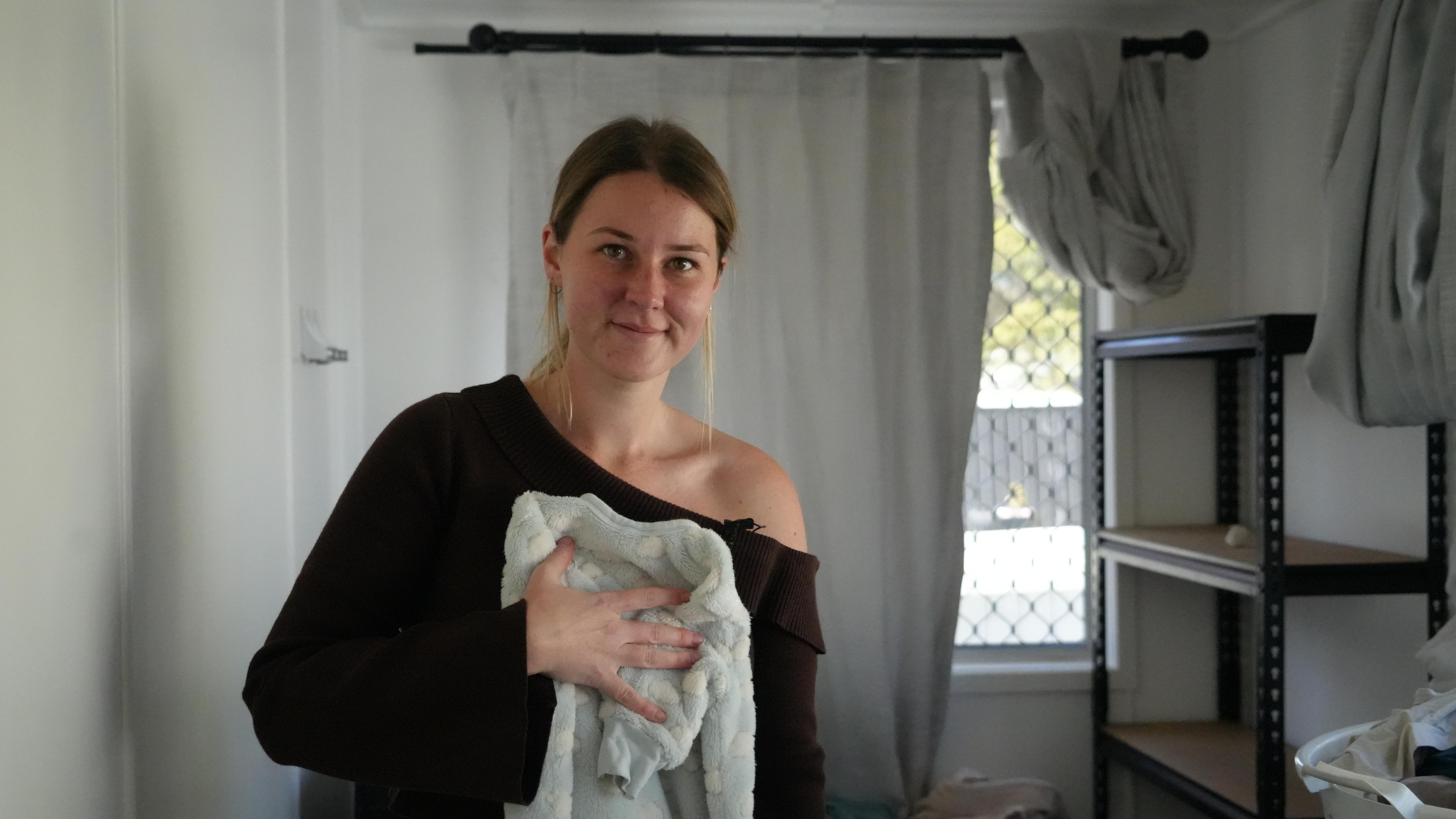 danica slack folding a onesie and smiling at the camera.