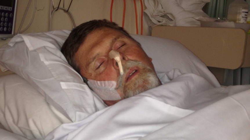 A man lies in a hospital bed in the dark with tubes in his nose