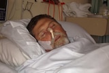 A man lies in a hospital bed in the dark with tubes in his nose