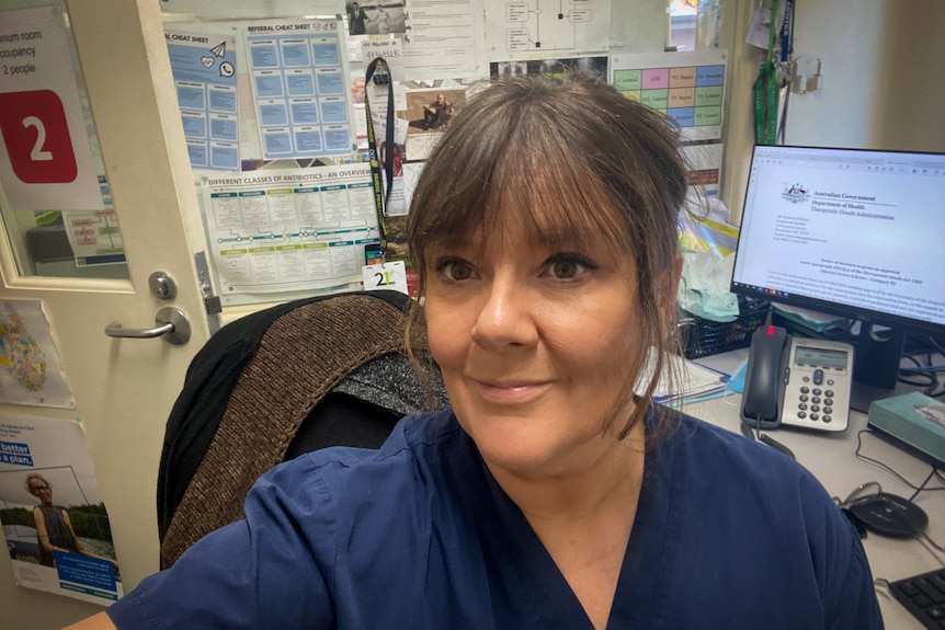 A nurse in blue scrubs in a clinical room