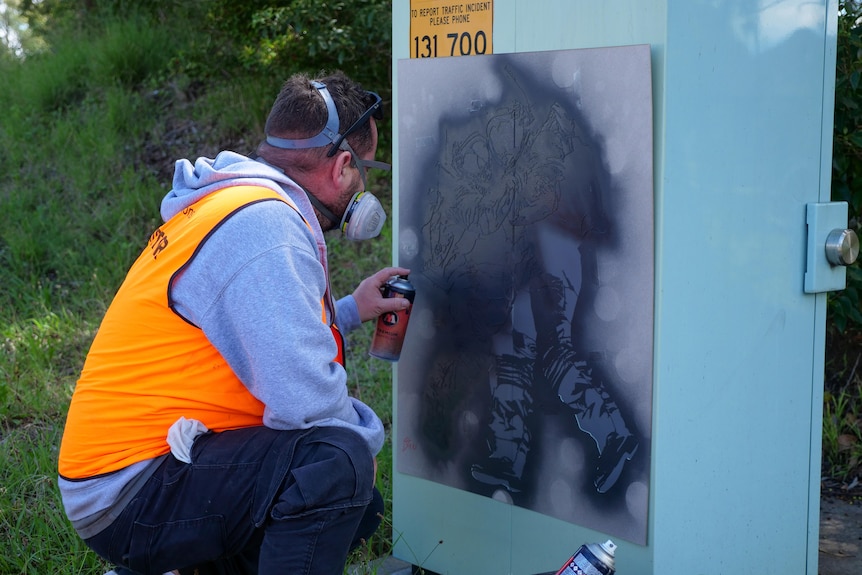 A man spray paints a roadside box. 