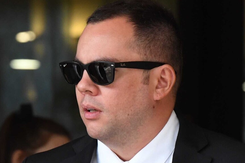 A man in a suit wearing a pair of black sunglasses.