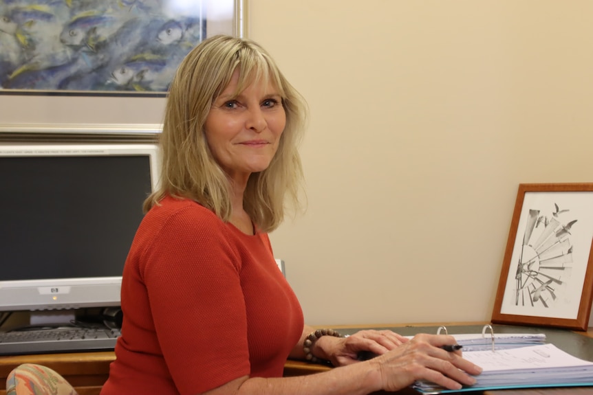 A smiling woman sitting at her desk inside an office.