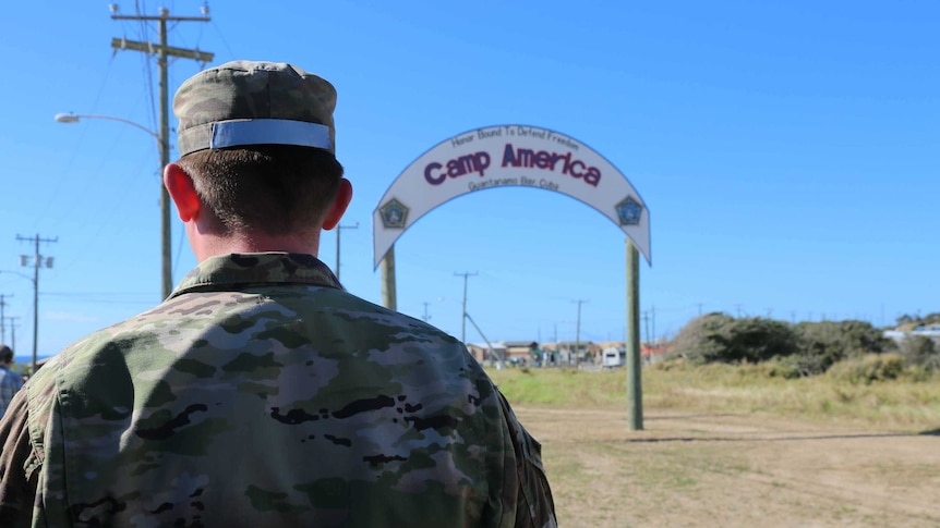 An unidentified soldier has his back to the camera and is facing a 'Camp America' sign