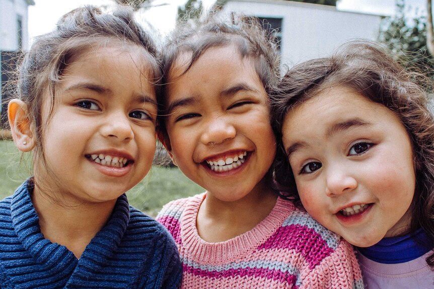 Three young girls smile while looking at the camera for a close-up photo.