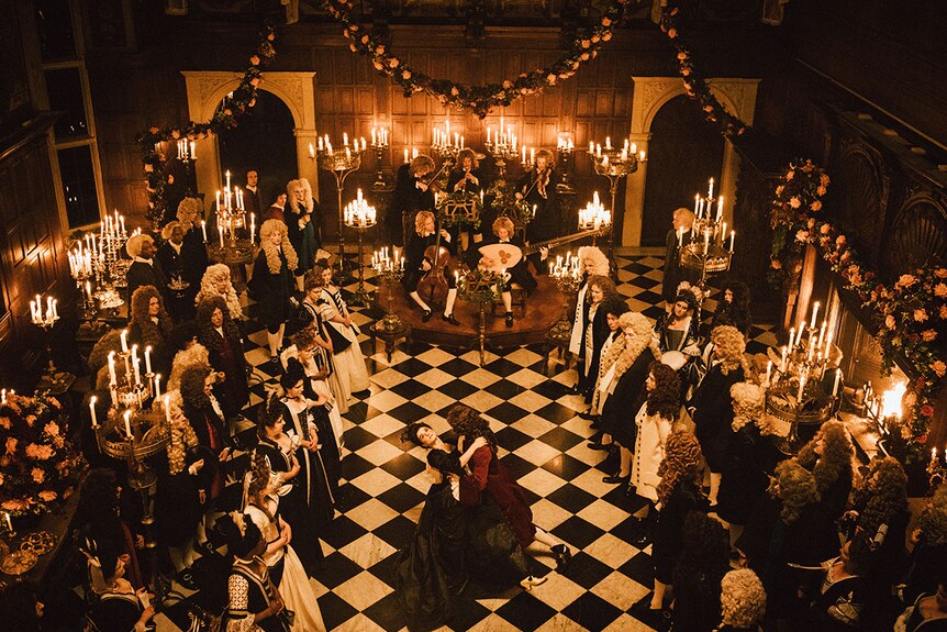 A grand hall with chequered black-and-white marble floor and filled people in 2018 film The Favourite.