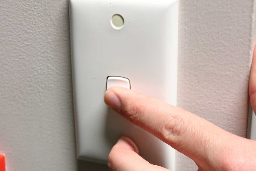 A hand turns on a light switch.