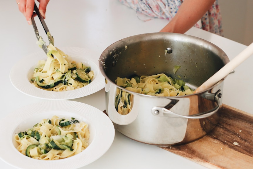 A woman serves a bowl of zucchini and leek pasta.