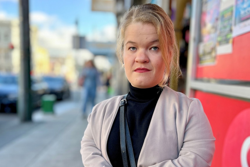 A white woman from the short statured community standing on a sidewalk. She has blonde hair 