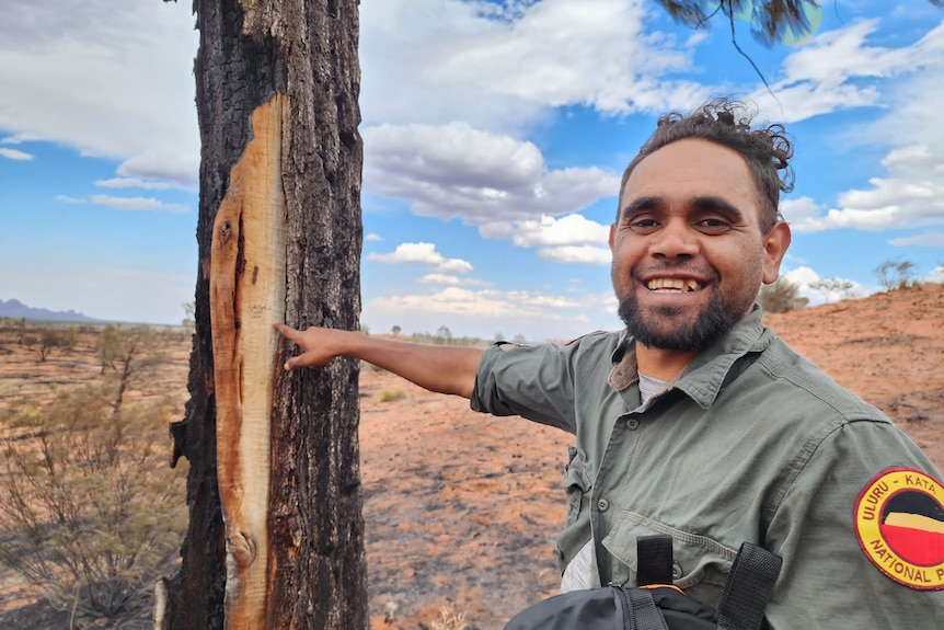 Ranger smiling in central australia desert beside a tree.