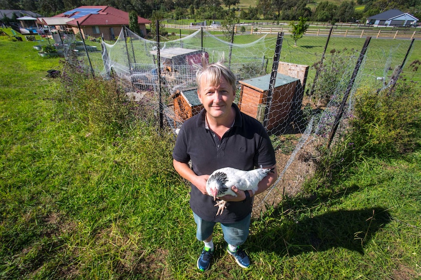 A man holding a white chicken in front of his chicken coop