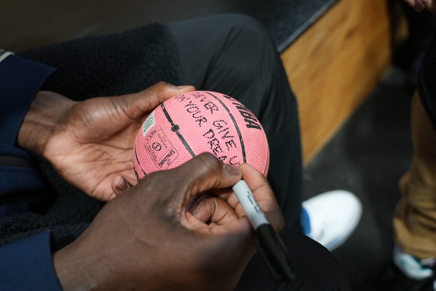 a small basketball is cradled in large hands as the words 'never give up on your dreams' are written on it with a black texter