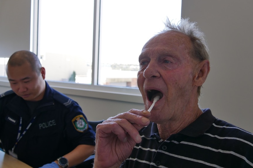 a man puts a stick in his mouth. There's a cop in the background