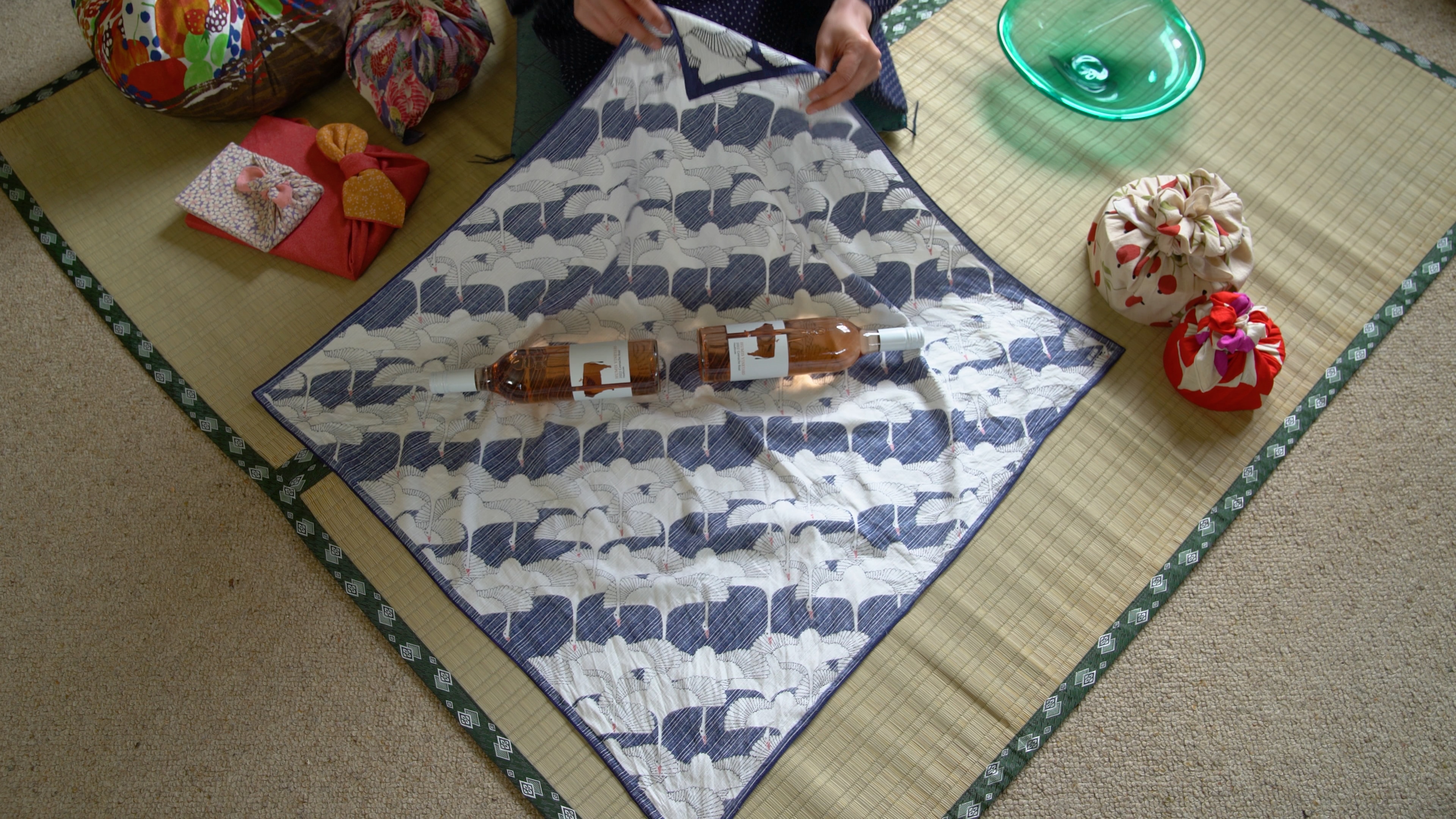 Two wine bottles facing opposite ends in the middle of a dark blue and white furoshiki fabric